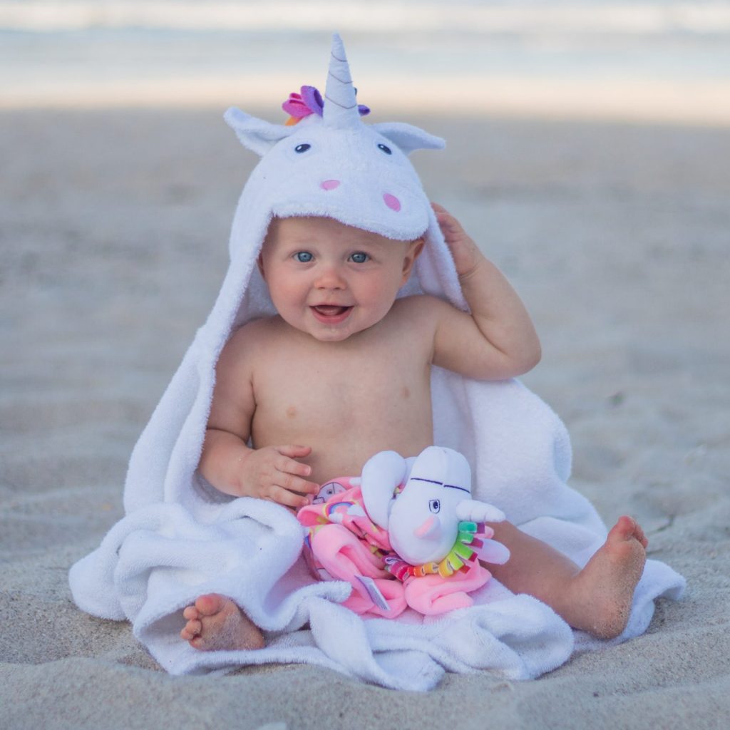 The Yikes Twins unicorn hooded towel for kids being worn by a young toddler at the beach